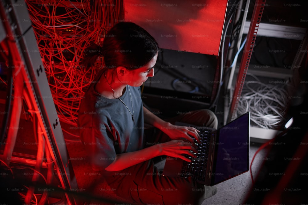 Blick aus einem hohen Winkel auf eine junge Frau in Militäruniform, während sie den Computer im Serverraum benutzt