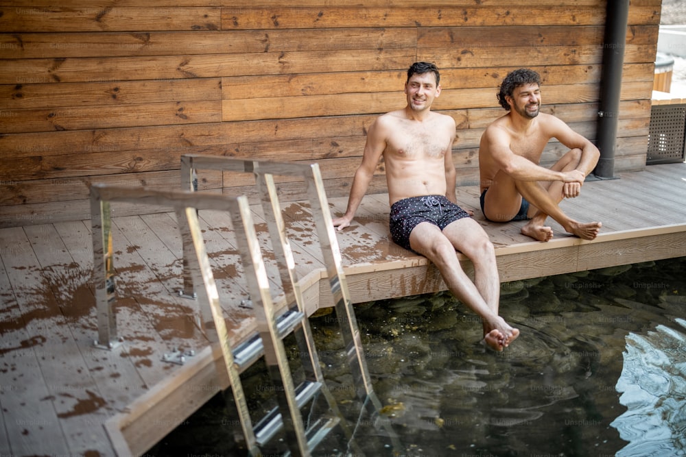 Amigos do sexo masculino sentados no terraço perto do lago no complexo de spa e conversando. Relaxe e divirta-se no spa de bem-estar.