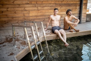Male friends sitting on the terrace near the lake in the spa complex and talking. Relax and fun time in wellness spa.