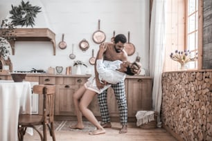 Lebensstil. Afroamerikanischer Mann ohne Hemd und hübsche Frau im Hemd barfuß tanzt am Morgen zu Hause in der Küche