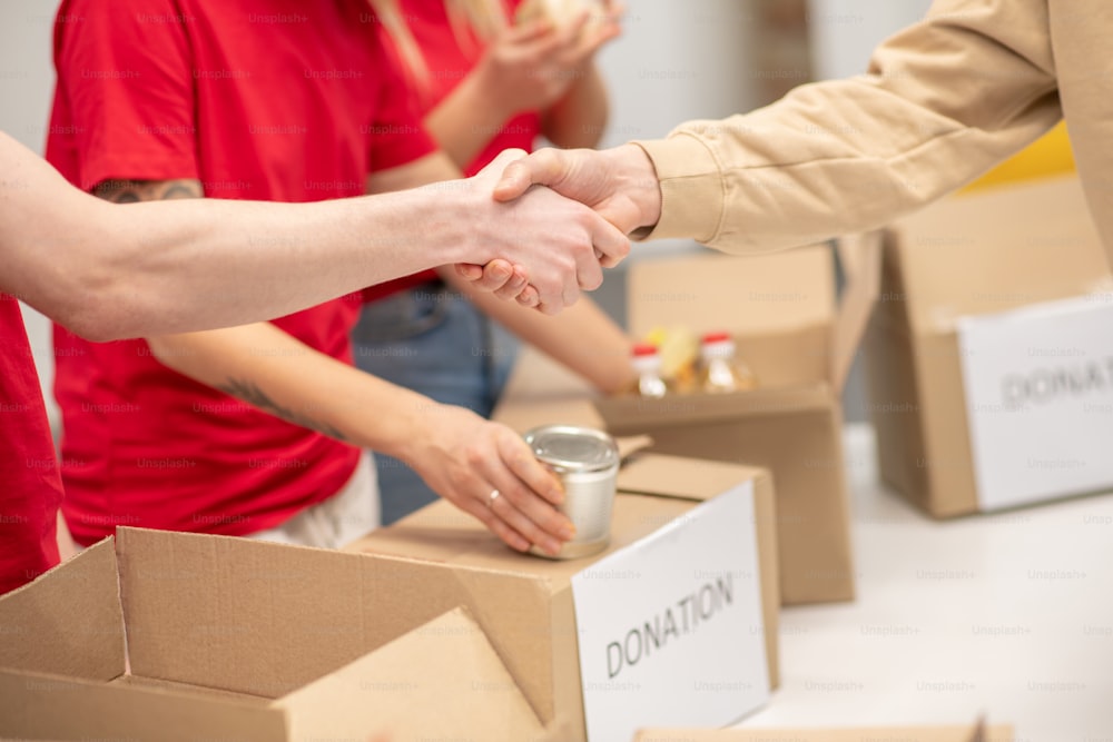 Geste de gratitude. Poignée de main en remerciement au bénévole et aux collègues derrière la distribution de dons au centre caritatif, pas de visages