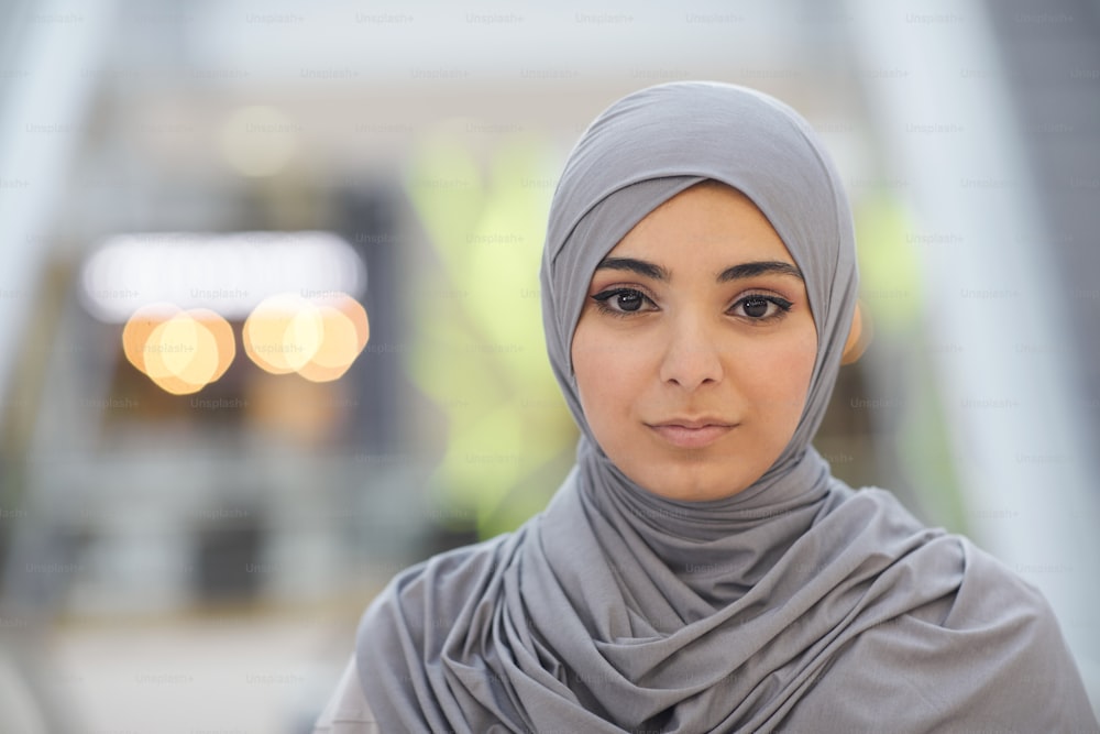 Close up portrait of beautiful Middle-Eastern woman wearing grey headscarf while standing in city with blurred background, copy space