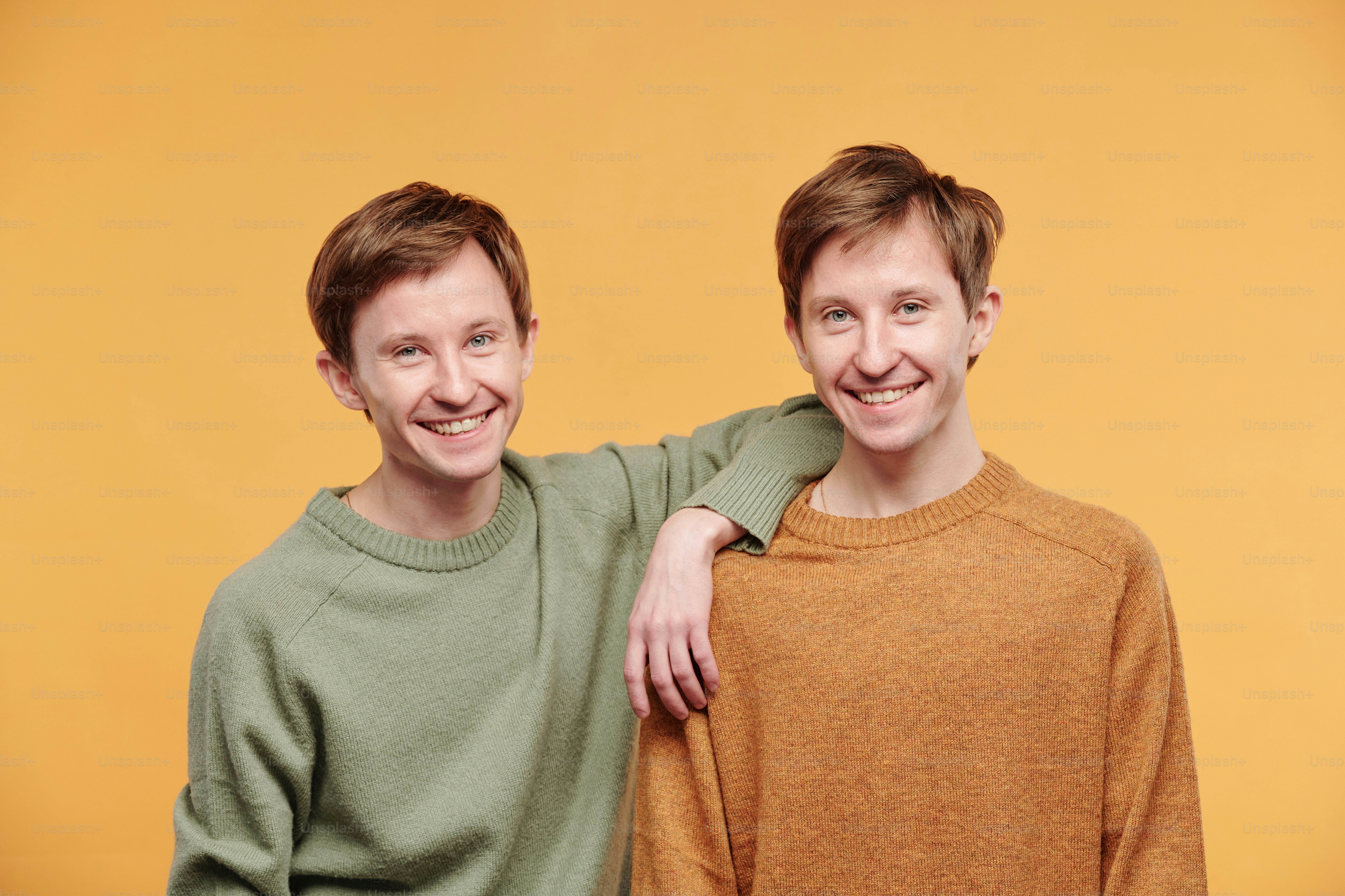 Ritratto di giovane felice in maglione casual appoggiato sulla spalla del fratello di interpolazione contro lo sfondo arancione