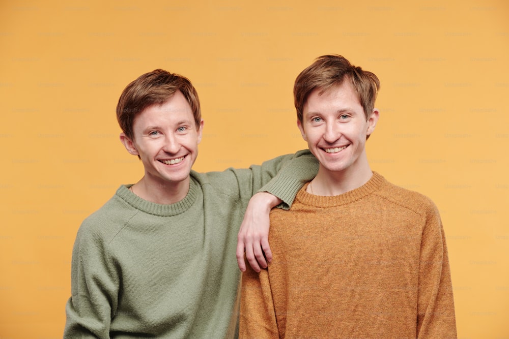 Retrato do jovem feliz no suéter casual apoiado no ombro do irmão pré-adolescente contra o fundo laranja