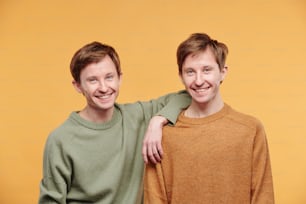 Portrait of happy young man in casual sweater leaning on shoulder of tween brother against orange background