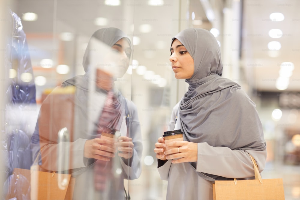 Retrato de vista lateral de una joven mujer de Oriente Medio con pañuelo en la cabeza y mirando escaparates mientras disfruta de las compras en el centro comercial, copie el espacio