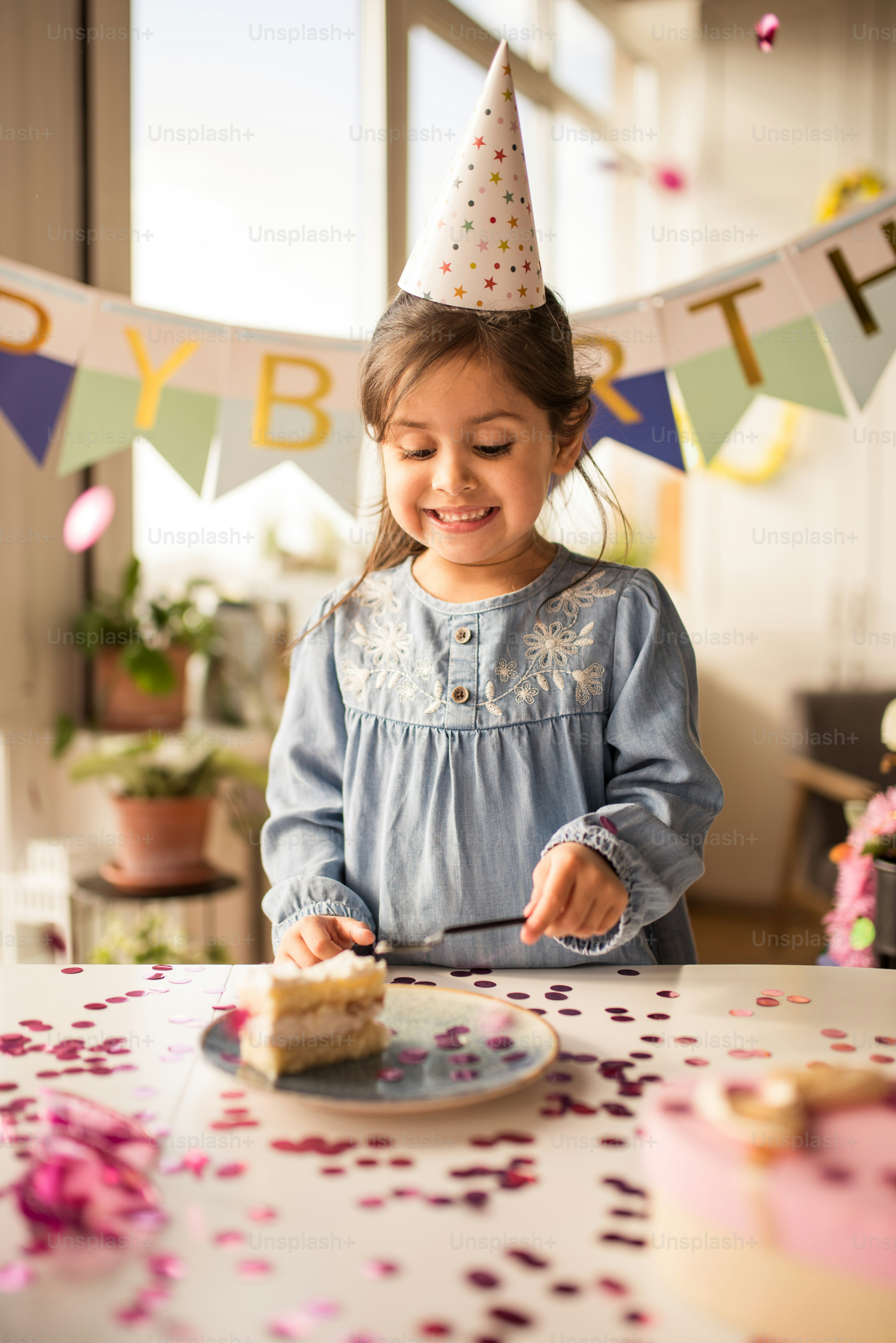 Waist up portrait view of the little happy girl eating her birthday cake with happy smile at the birthday party at home during the quarantine. Stock photo