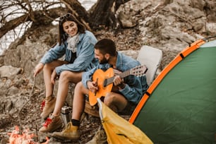 Romantic couple sitting by bonfire. Beautiful couple in love enjoying at campsite.