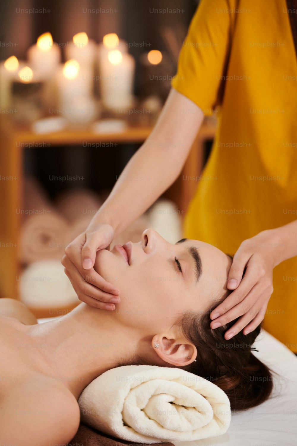 Close-up da mulher deitada com os olhos fechados enquanto o terapeuta massageia seu rosto