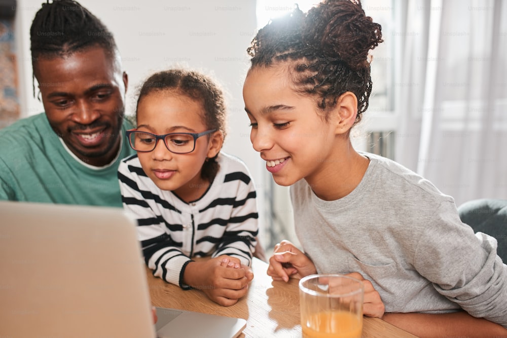 So interesting. Portrait view of the happy friendly family looking with interest at the laptop screen while sitting at the morning at the table and feeling great. Stock photo