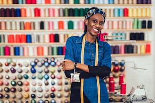 Portrait of happy african fashion designer woman in studio. Background of colorful sewing thread.