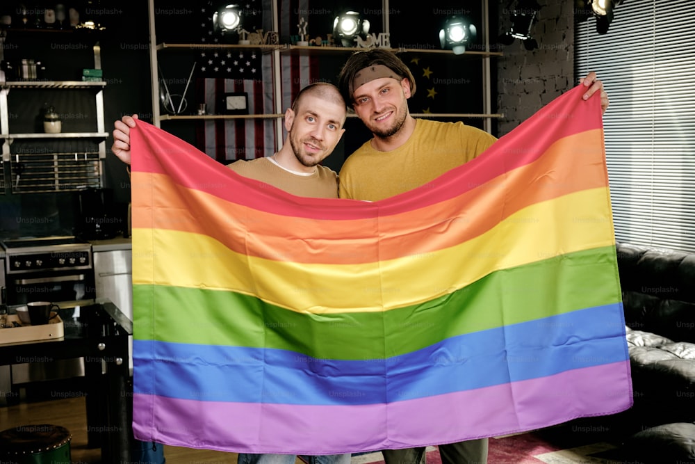 Giovane coppia omosessuale affettuosa che tiene la bandiera arcobaleno