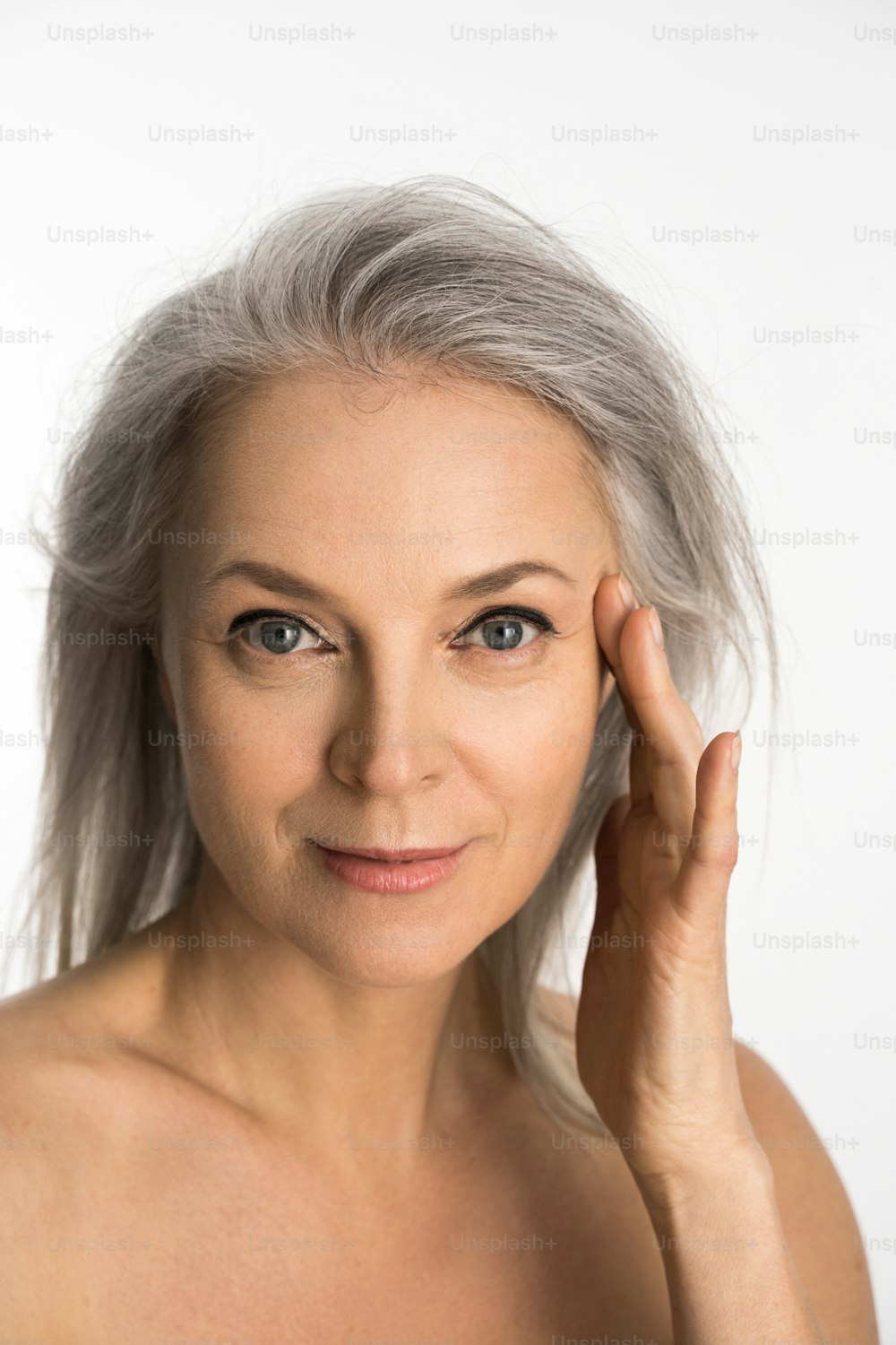 Charming old woman touching her perfect soft face skin with fingers and smiling to the camera over white background. Woman using day or night face cream. Cosmetology procedures concept