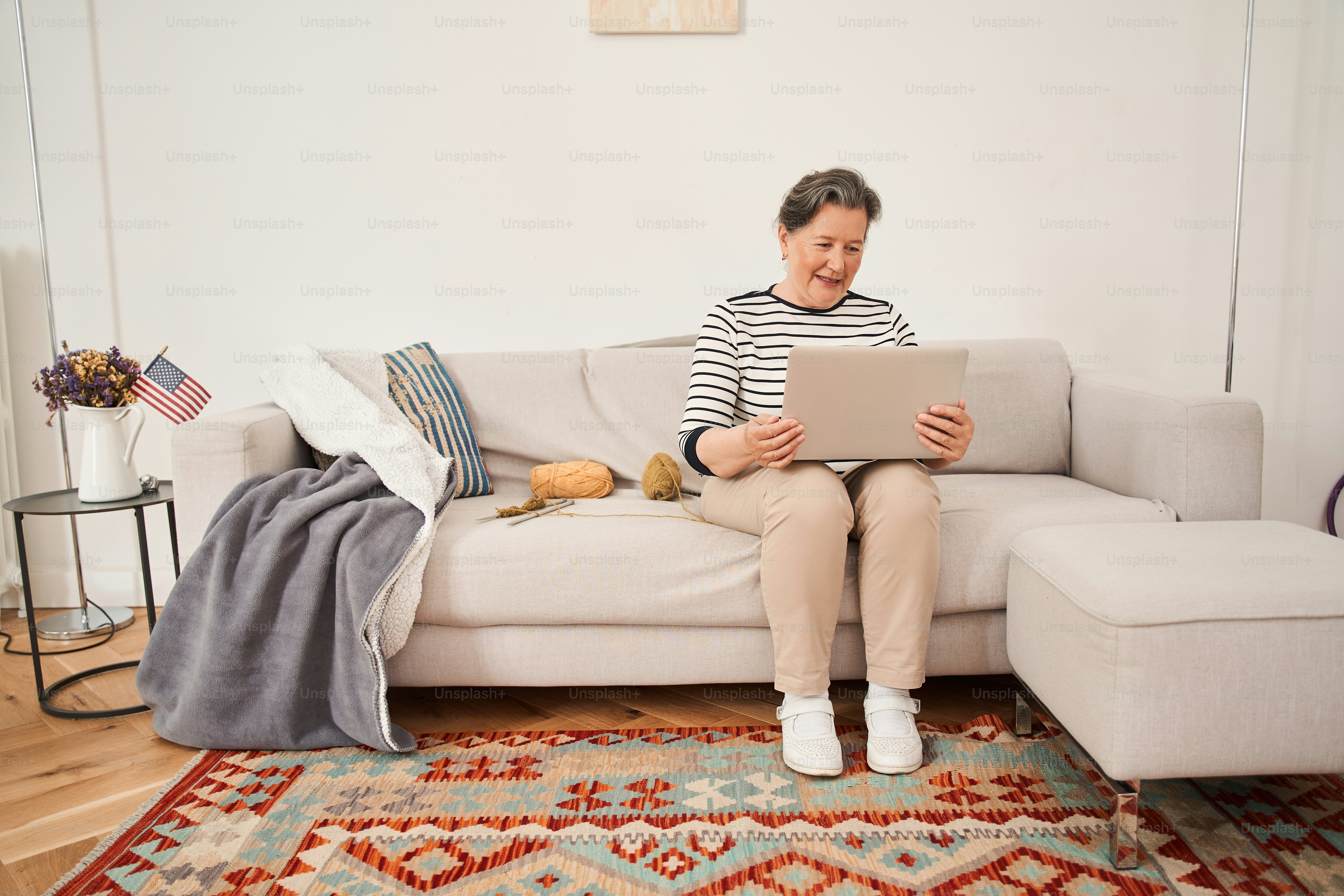 Full length view of the senior woman holding video call with her family or friends from the laptop while spending pastime at the retirement house