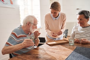 Time for the medicine. Friendly caregiver giving medicine for senior man and woman while working at the retirement house. Stock photo