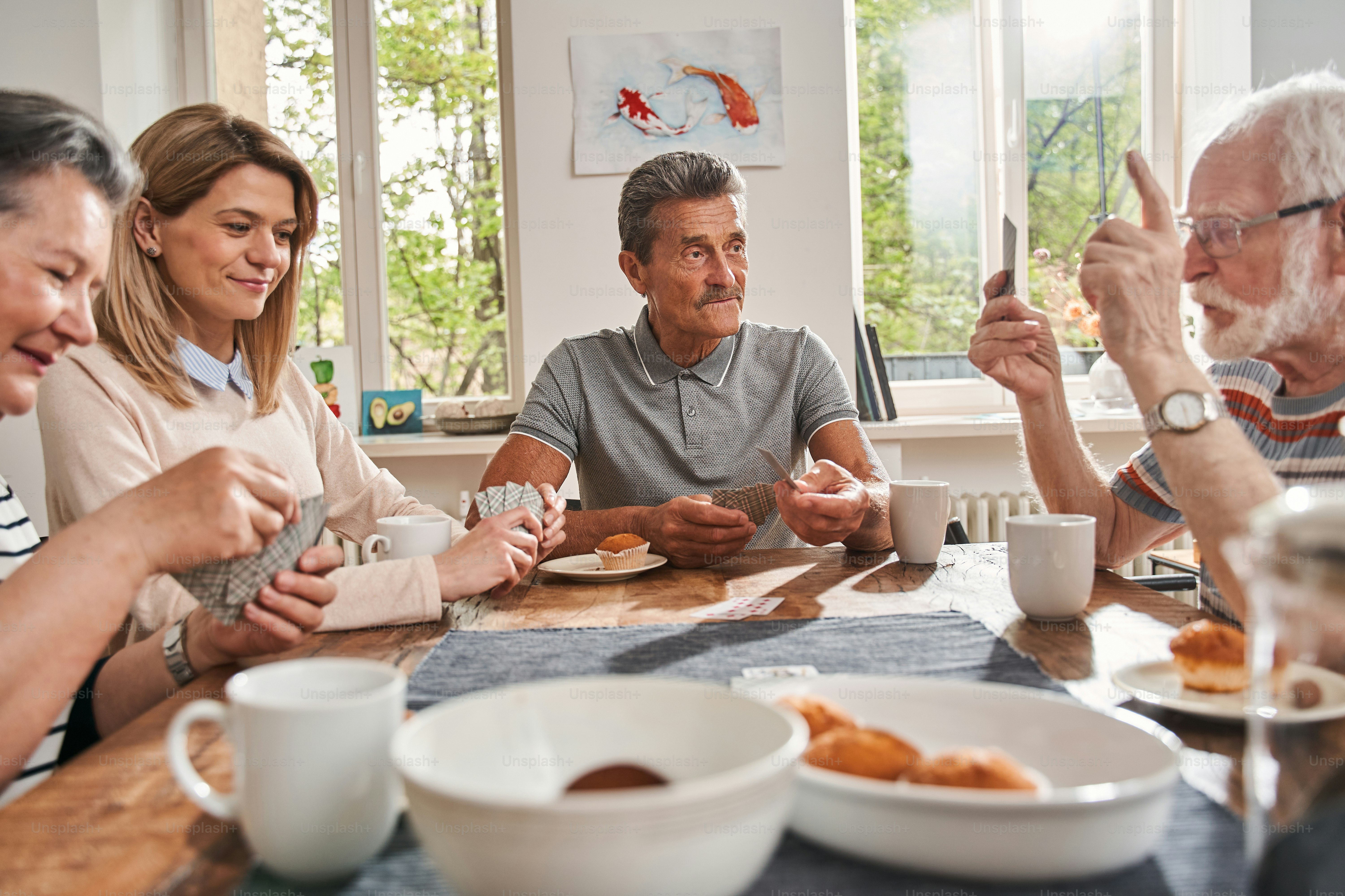 Waist up portrait view of the group of senior people sitting by the table in a nursing home and chatting with each other with interest. Stock photo