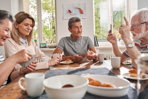 Vista retrato do grupo de idosos sentados à mesa em uma casa de repouso e conversando uns com os outros com interesse. Foto de Stock