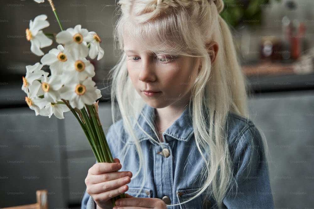 Adoro i fiori. Vista ritratto della calma ragazza bionda in piedi al tavolo e pronta a mettere fiori al vaso in cucina. Concetto di comfort domestico