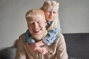 Childhood. Cute small girl feeling satisfied and happy while spending day with her father. Strong albino father embracing with his lovely daughter and looking at the camera