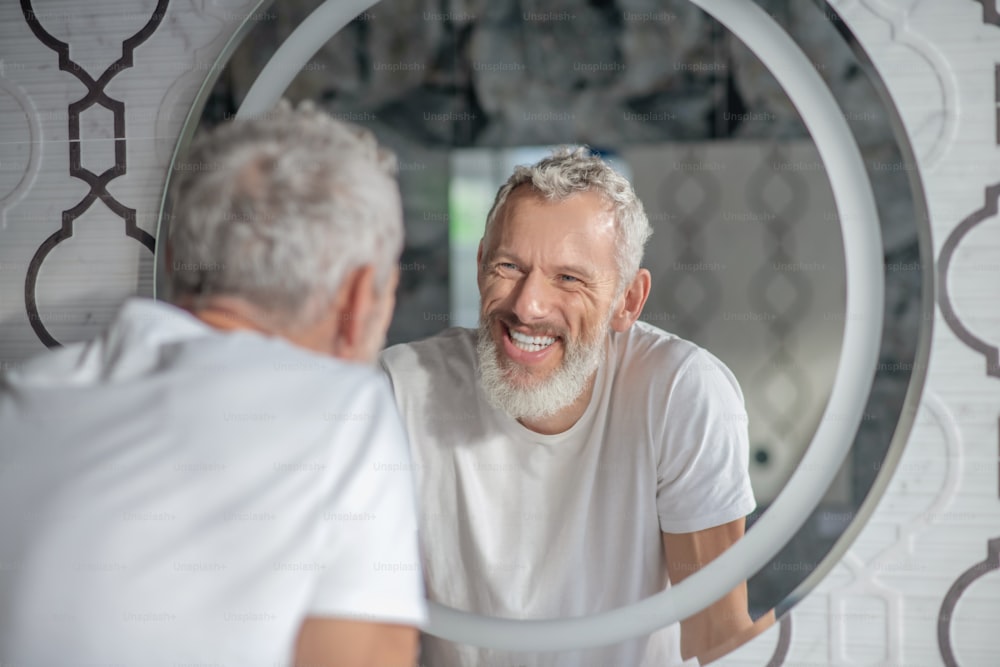 Ser legal. Um homem sorridente de cabelos grisalhos olhando para o espelho