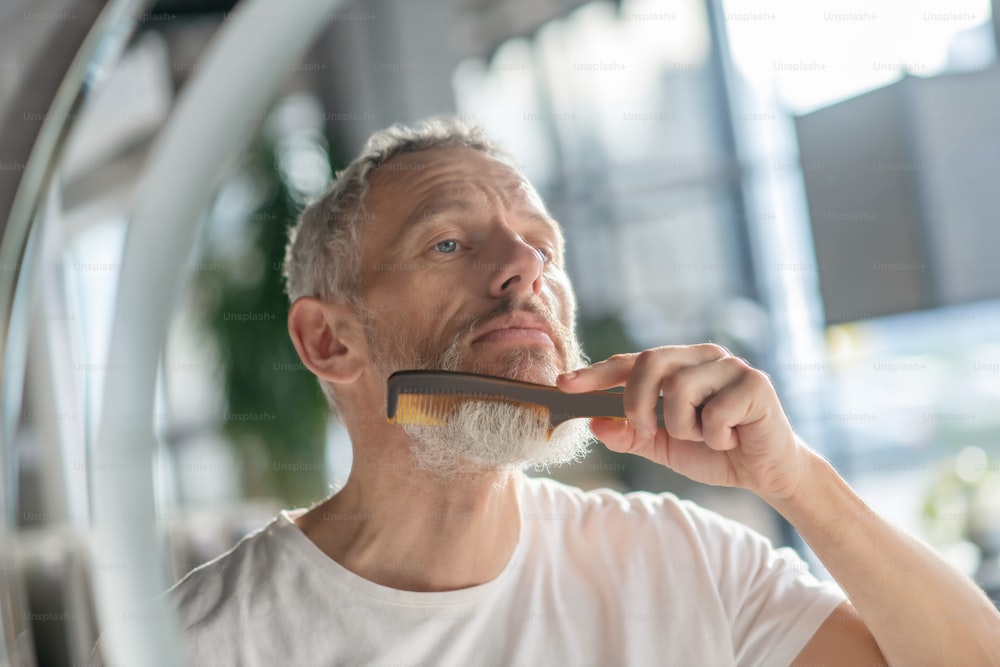 Fixing beard style. A man styling his beard with a comb