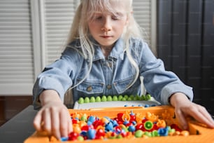 So interesting. Waist up portrait view of the little albino child girl looking at the details of her game while folding it at the table. Leisure games concept