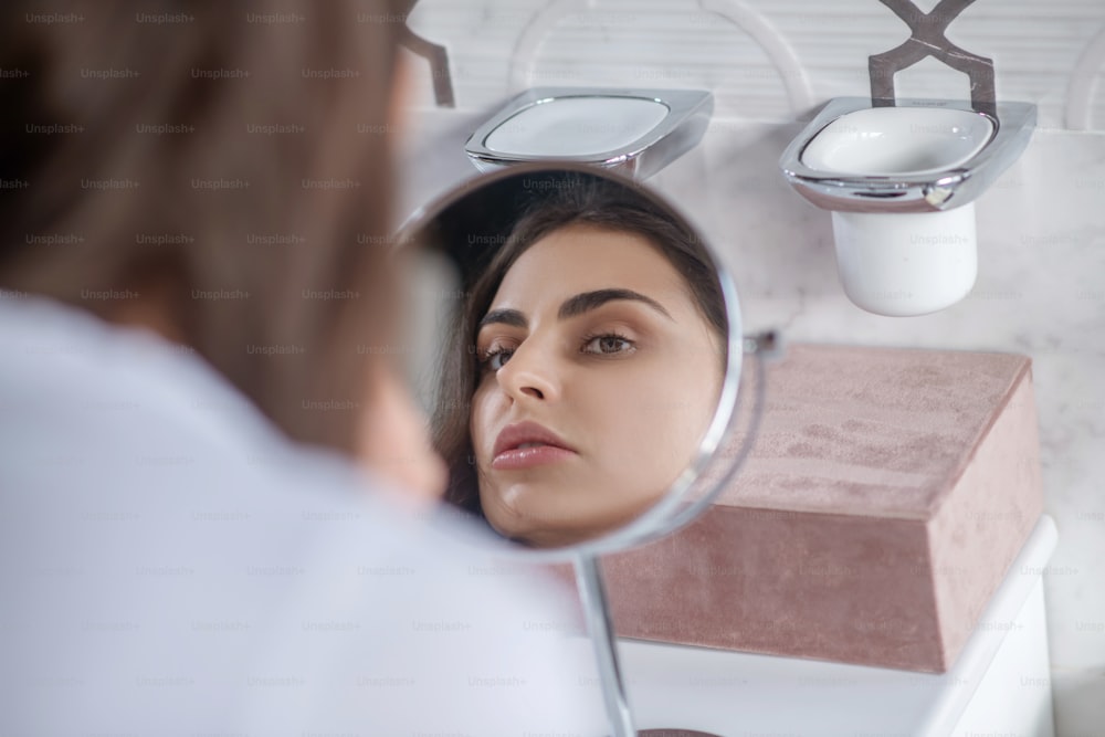 Beauty procedures. A beautiful woman looking at the small mirror