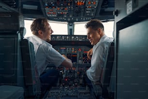 Vista traseira de um capitão de companhia aérea alto astral e um primeiro oficial sentado no convés de voo