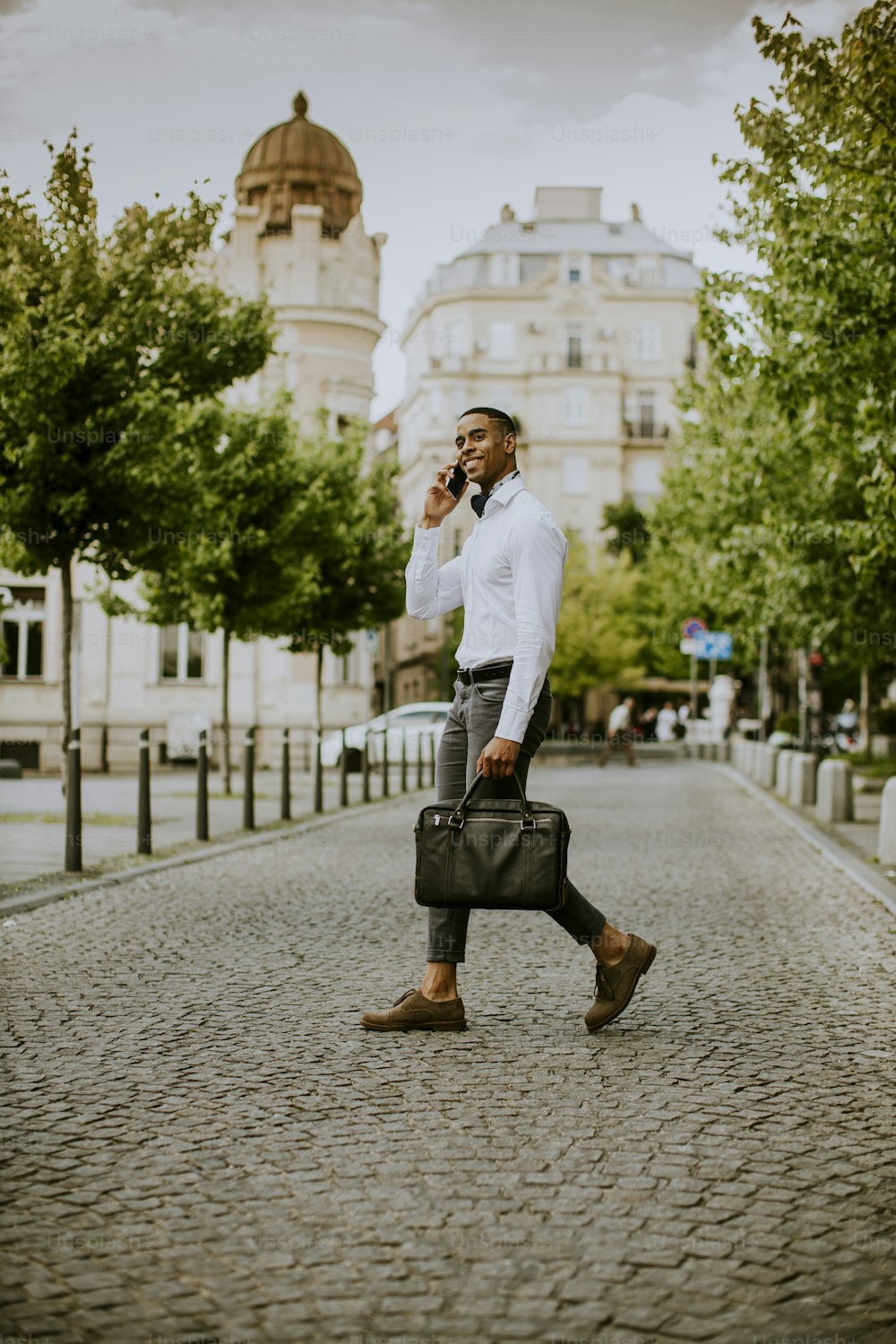 Handsome young African American businessman using a mobile phone while ceossing a street