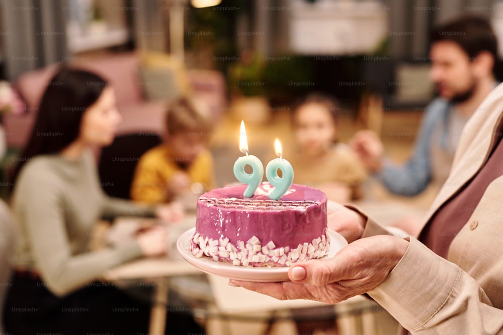 hand of mature woman holding birthday cake with two nine-shaped candles