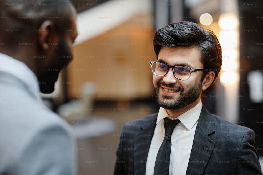 Portrait of smiling Middle-Eastern businessman talking to partner while standing in hotel lobby