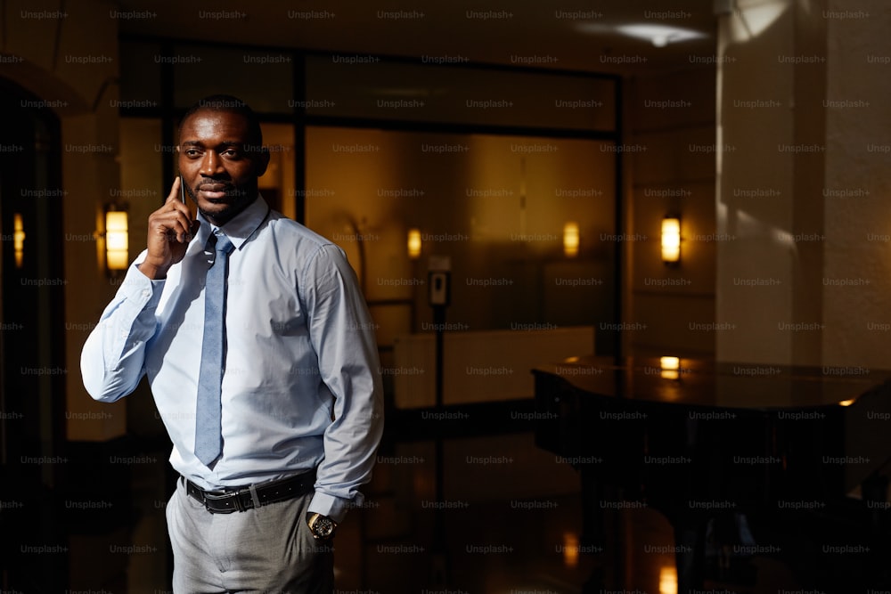 Waist up portrait of handsome African-American businessman speaking by smartphone in sunlight, copy space