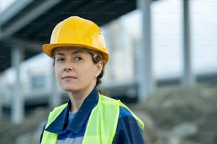 Young female builder in hardhat and uniform on construction site