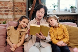 Mature female reading book with her grandchildren in living-room