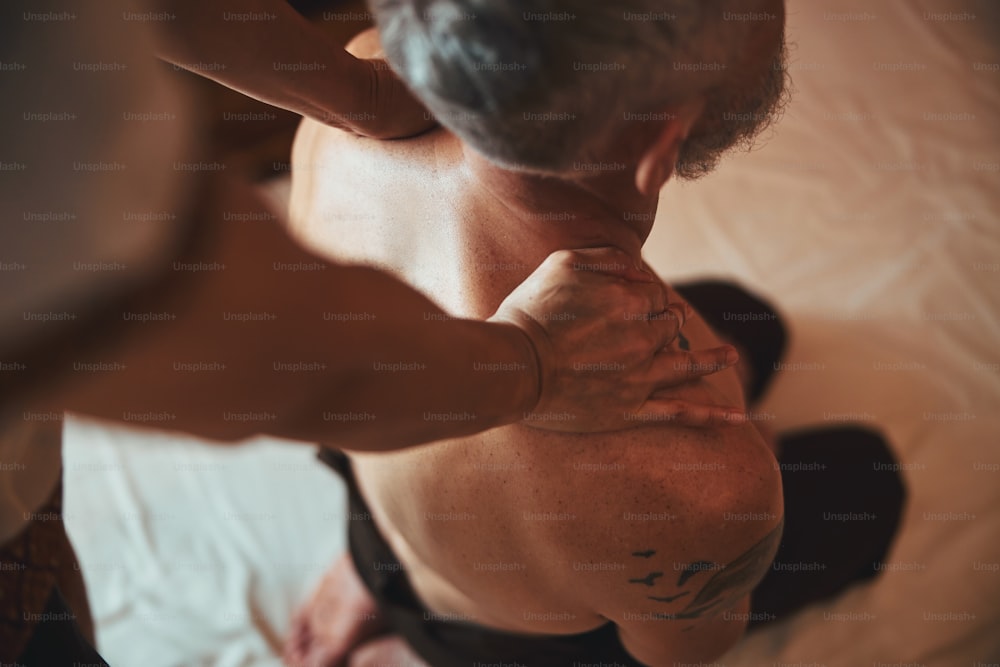 Draufsicht abgeschnittener Kopf von Frauenhänden, die Massage auf grauen männlichen Schultern im thailändischen Spa machen