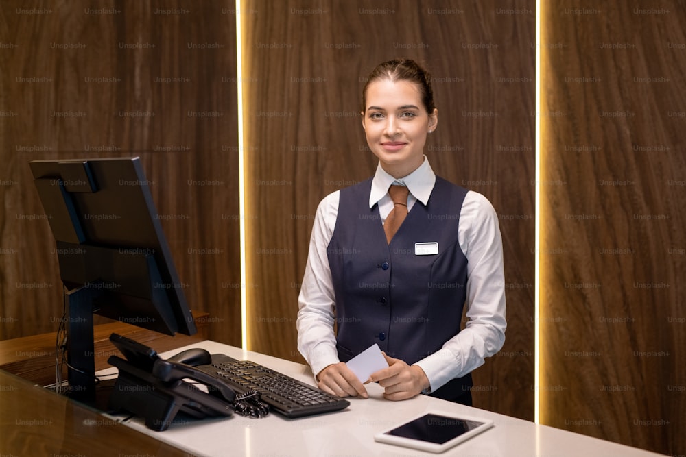 Happy young receptionist in uniform standing by counter