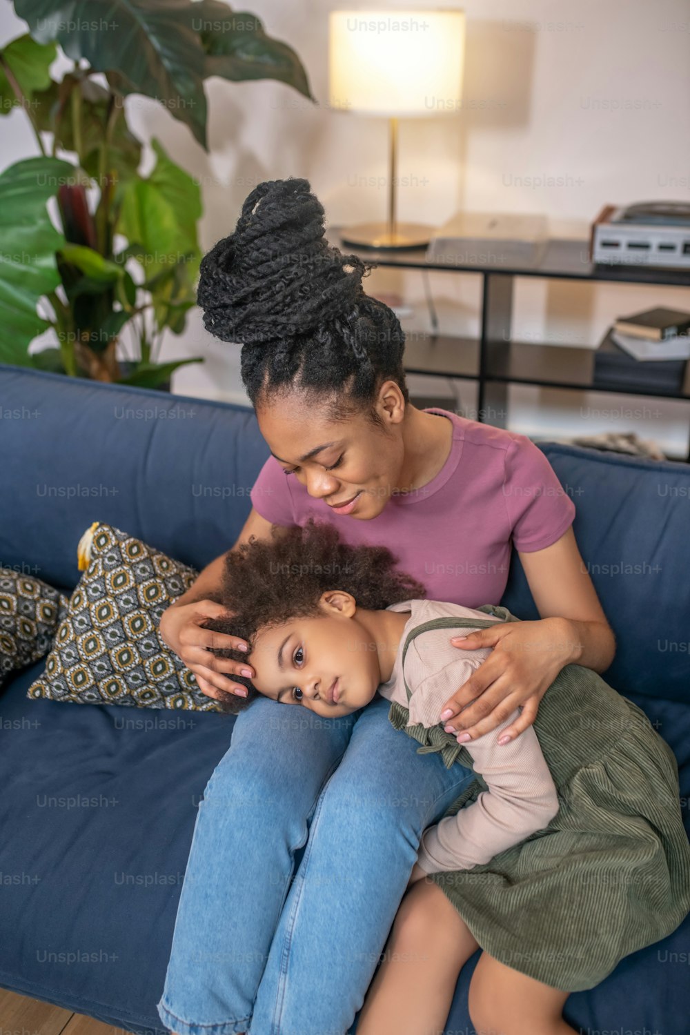 Mom, concern. Attentive african american mother gently hugging tired little girl on sofa in cozy room