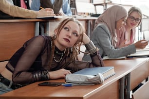 Adolescente femminile distratta che giace sulla scrivania a lezione mentre altri lavorano