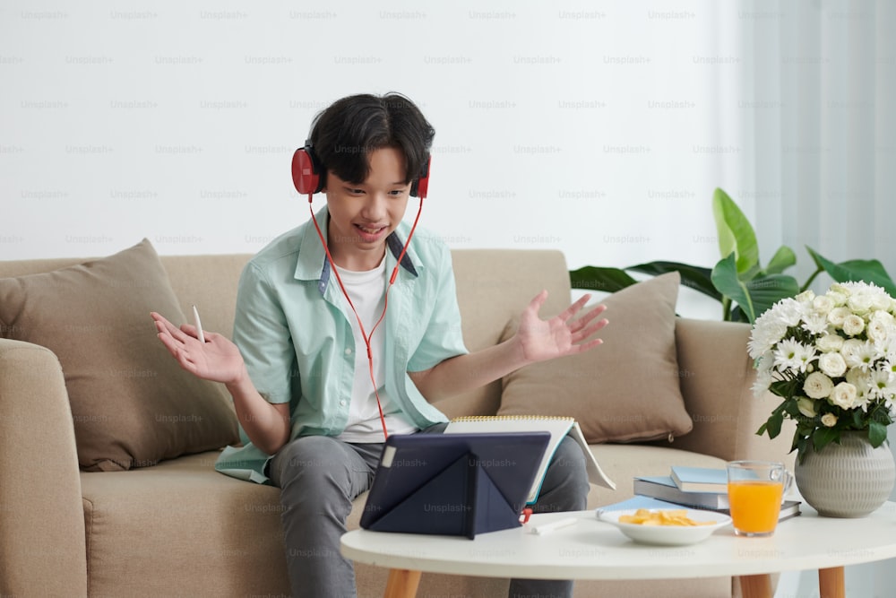 Excited teenage boy in headphones video calling friend to discuss homework or school project