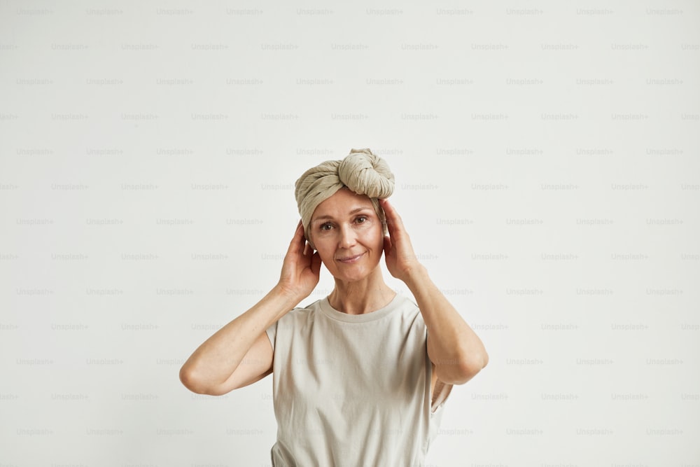 Minimal waist up portrait of beautiful mature woman wearing headscarf and dress looking at camera dreamily, copy space