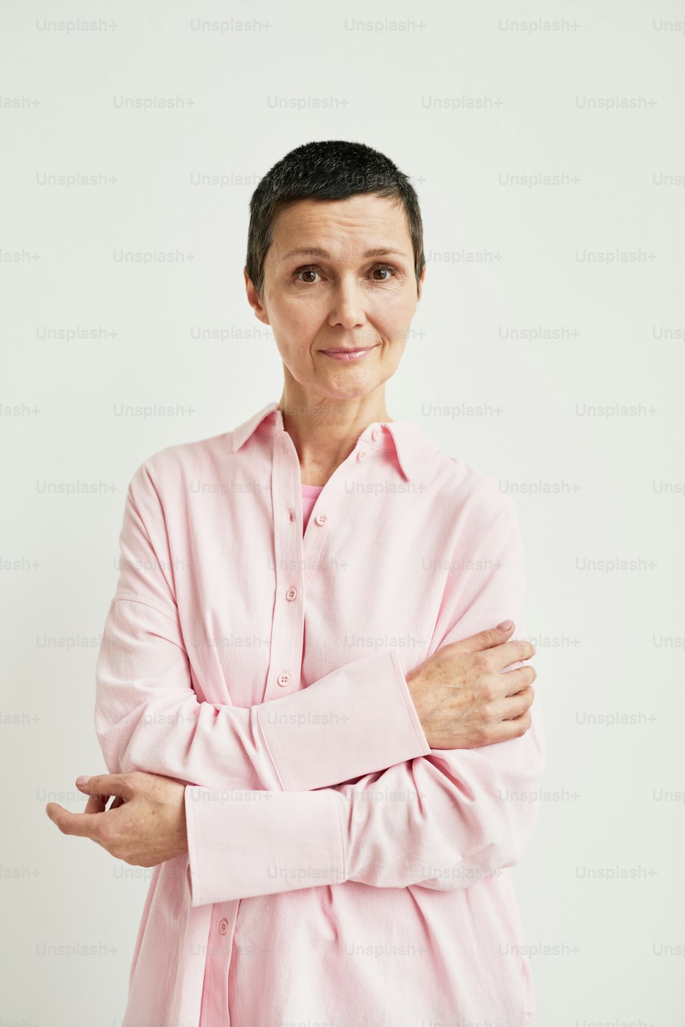 Ritratto minimale di donna matura sicura di sé con taglio di capelli corto che guarda la macchina fotografica mentre indossa la camicia rosa