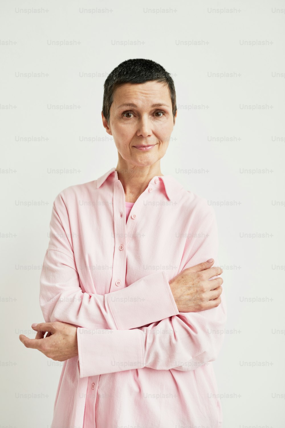 Minimales Porträt einer selbstbewussten reifen Frau mit kurzem Haarschnitt, die in die Kamera schaut, während sie ein rosa Hemd trägt