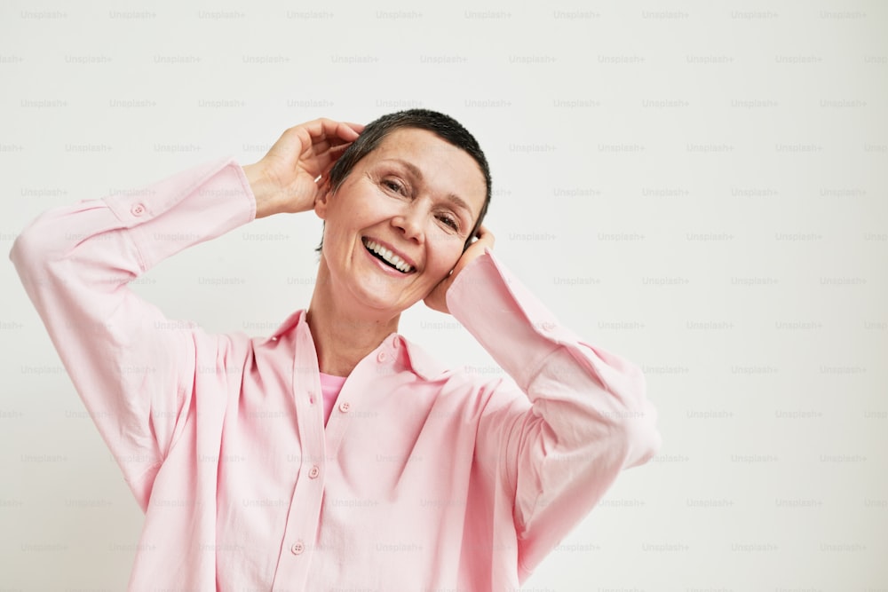 Minimal portrait of carefree mature woman with short haircut looking at camera while wearing pink dress shirt