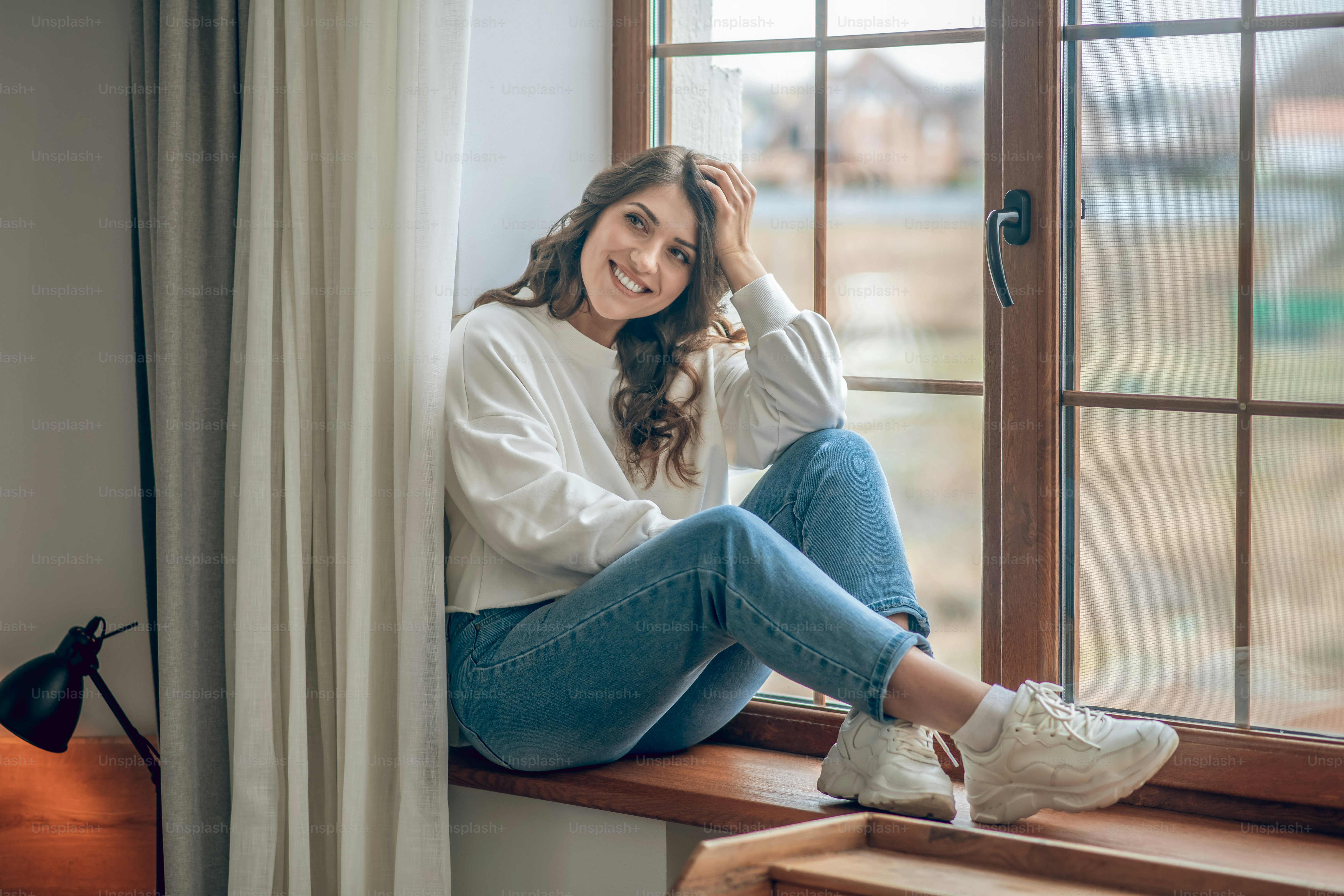 午前中に。白いブラウスを着たかなり若い長髪の女性が窓際に座って思慮深く見える