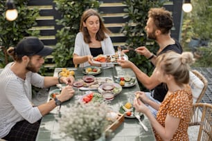 Un pequeño grupo de jóvenes amigos almuerza al aire libre, come verduras y pescado a la parrilla y se divierte en el patio trasero