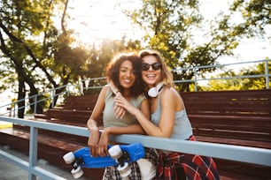 Zwei fröhliche junge Mädchen mit Skateboard haben Spaß zusammen im Park