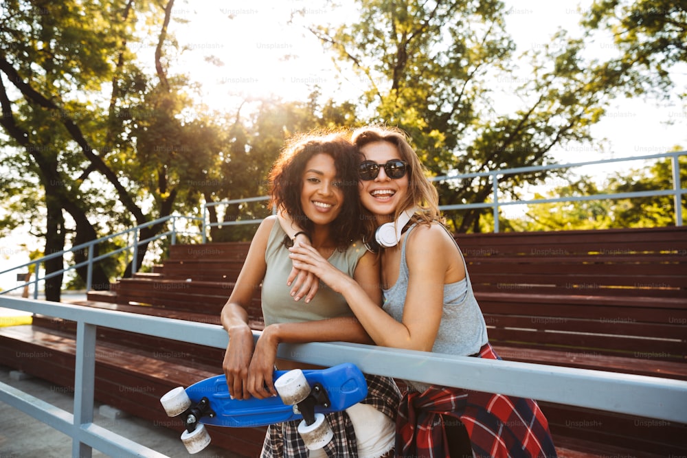 公園で一緒に楽しむスケートボードを持つ2人の陽気な若い女の子