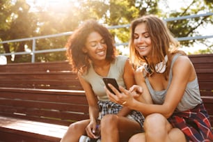 Due ragazze entusiaste che si divertono insieme mentre usano il telefono cellulare al parco