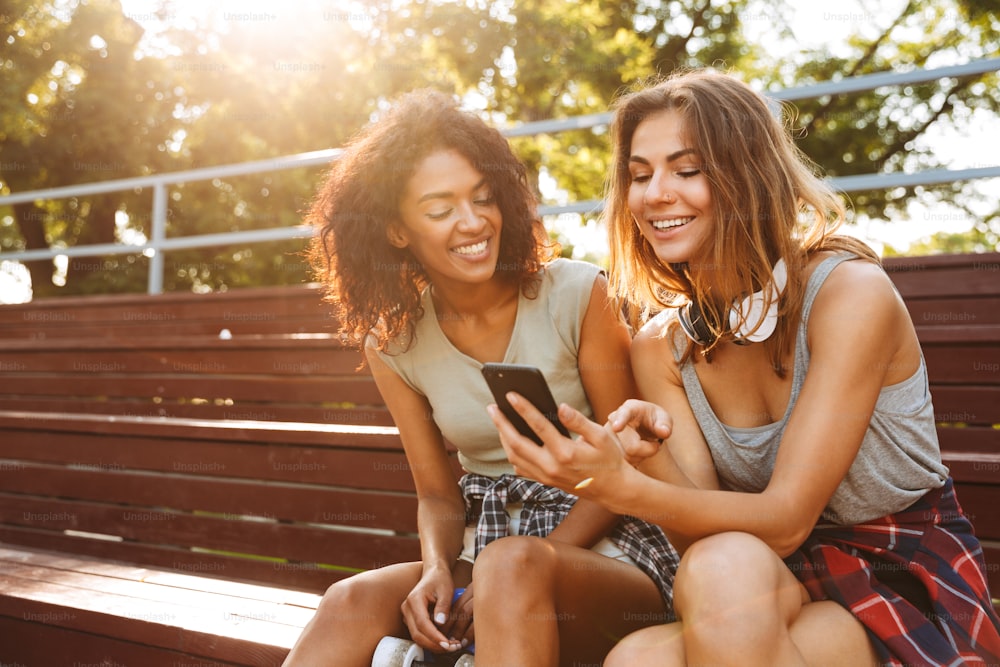 Two excited young girls having fun together while using mobile phone at the park