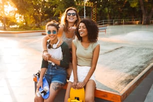 Three cheerful pretty young girls having fun with skateboards at the park
